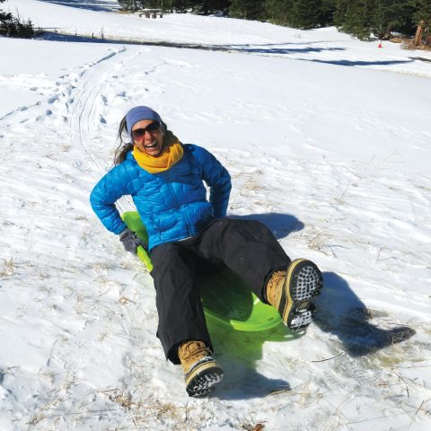 woman laughing while riding on a sled in snow