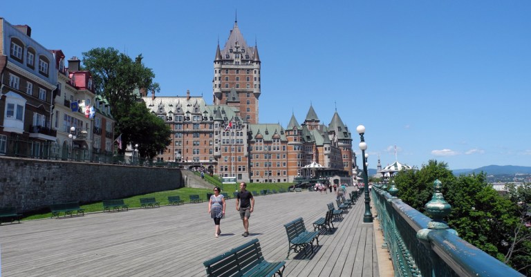 a couple walking along a boardwalk with an historic hotel in the background