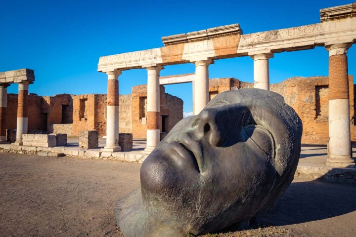 Ruins and a large bronze head in ancient Pompeii city, Italy.