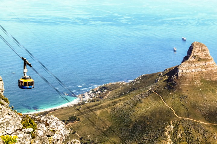 Top down view from Table Mountain of a cable car and the Lion's Head on the right and Atlantic Ocean in the background