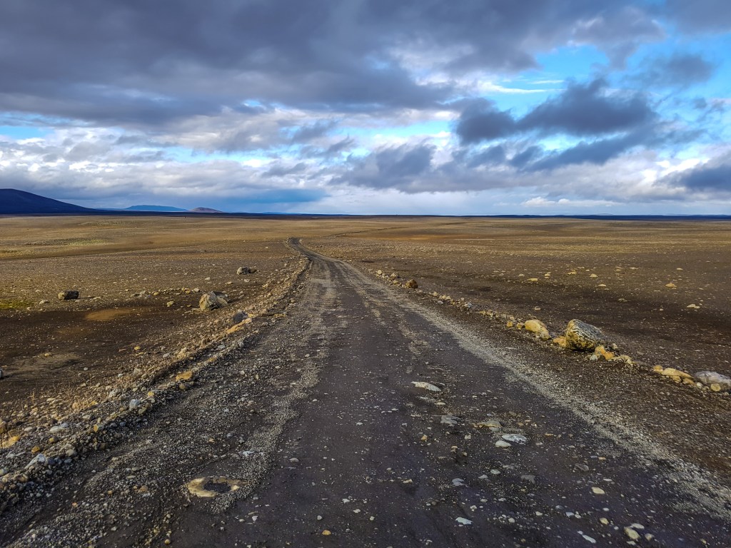 A rocky dirt road and vast tundra plain under moody purple and blue sky.