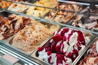 Various flavors of gelato with toppings in a glass display case